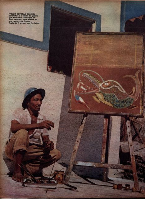 Colour magazine page: a man in a blue hat crouches barefoot beside a wooden easel against a whitewashed wall, his brushes and paint tins on the ground; on the easel, a painting of a large fish with an open toothed mouth swallowing smaller fish.